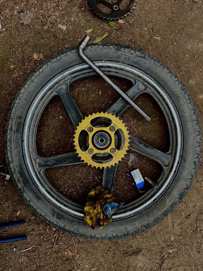Motorcycle wheel with sprocket and tools on dirt ground in DIY repair setup.