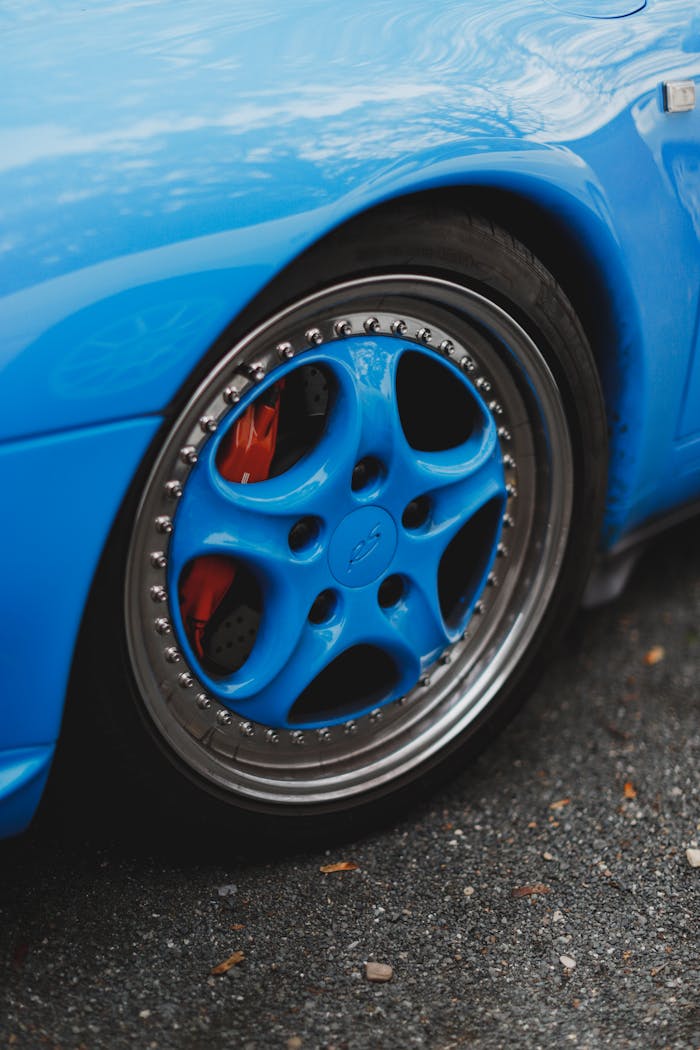 Detailed shot of a blue custom car wheel with visible red brake caliper on a wet road.