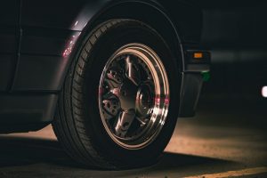Detailed shot of a classic car wheel in dim lighting, emphasizing the sleek design and metallic finish.